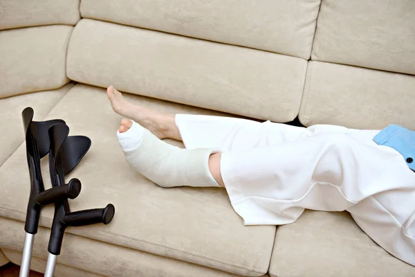 stock image Closeup photo of broken female leg. Elbow crutches and orthopedic plaster. White ankle and foot splint bandages on the leg. Young woman's fall accident. Injury, trauma, recovery concept. Copy space