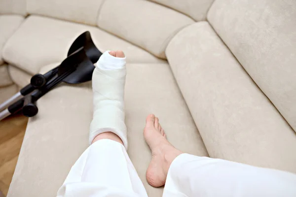 Closeup photo of broken female leg. Elbow crutches and orthopedic plaster. White ankle and foot splint bandages on the leg. Young woman\'s fall accident. Injury, trauma, recovery concept. Copy space