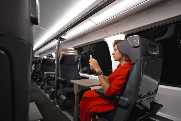 Businesswoman with ginger hair on train traveling to another city for an important meeting. Woman traveling with social distance for pandemic protection enjoying 5g mobile connection in train wagon.