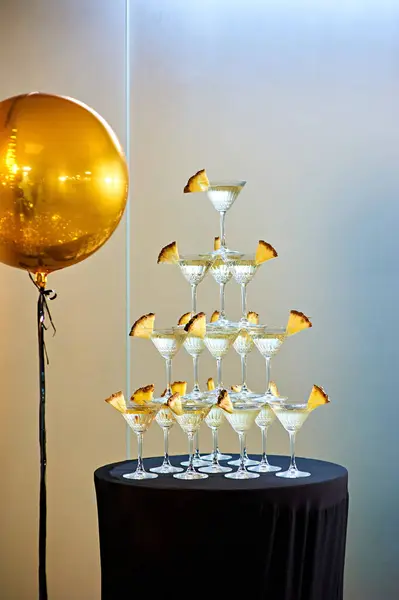 Pyramid-shaped pineapple-filled champagne glasses on a black table near photobooth. Light dances off the crystal, creating an atmosphere of luxury and celebration. New Year or Christmas Party.