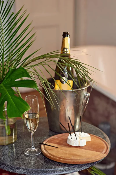 ブリーチーズとシャンパンの隣のテーブルのグラス アイスバケツのシャンパンのボトルとヤシの葉の花瓶 テイスティング 2人のためのロマンチックな夜 ストックフォト