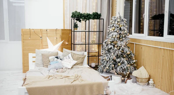 クリスマスの寝室のインテリアを飾りました 雪に覆われた効果と光沢のある金の装飾を持つクリスマスツリー クリスマスツリーの下にプレゼント 枕付きの居心地の良いベッド お祝い 新年のインテリアデコレーション ストックフォト