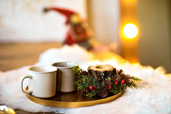 2つのカップ サンジャ 赤い果実の配置とトレイのクローズアップ そして白い毛皮の敷物にコーン バックグラウンドで輝くエルフ 居心地の良いクリスマスの雰囲気 暖かい飲み物でのお祝いの夜 ロイヤリティフリーのストック画像