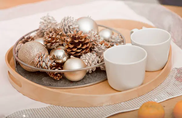 2つのカップの配置と光沢のある銀製のクリスマスの装飾と白いテーブルクロスの松のコーンの構成でトレイのクローズアップ 新しい年とクリスマスの装飾のアイデア スティルライフ ストック画像