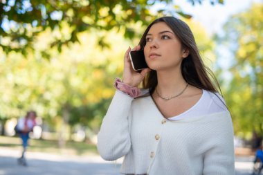 Parkta yürürken akıllı telefonuyla konuşan genç bir kadın.