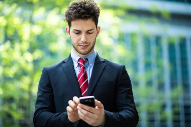 Açık havada akıllı telefon kullanan yakışıklı genç bir yönetici.