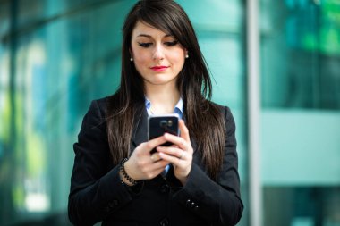 Güzel genç bayan yönetici dışarıda akıllı telefonunu kullanıyor.