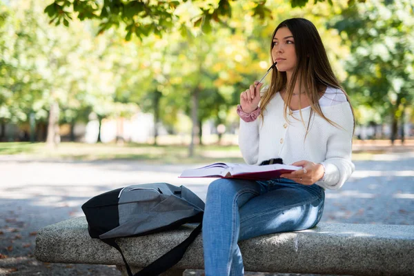 公園のベンチの屋外に座って本を勉強する女子大生 — ストック写真