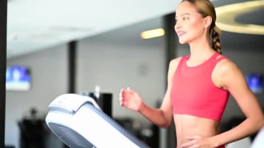 Spor salonundaki koşu bandında antrenman yapan güzel bir kadın, sonunda gülümsüyor.