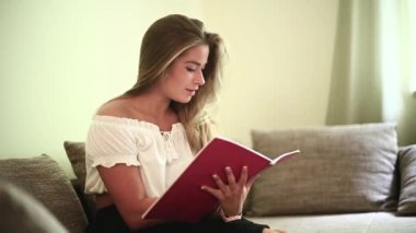 Genç bir kadın dairesindeki kanepesinde oturmuş ders çalışıyor.