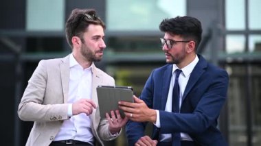 İki işadamı sokakta tabletle meşgul bir şekilde sohbet ediyorlar.