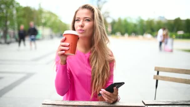 快乐的年轻女人一边在户外喝咖啡一边用智能手机 — 图库视频影像