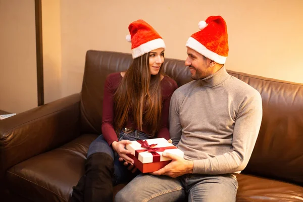 Junges Paar Mit Nikolausmütze Hält Weihnachtsgeschenk Hause — Stockfoto