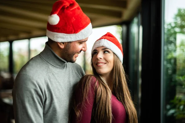 Schönes Paar Umarmt Sich Mit Nikolausmützen Fenster — Stockfoto