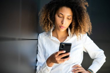 Güzel, genç, Afro-Amerikan bir menajer. Açık havada akıllı telefonunu kullanıyor.