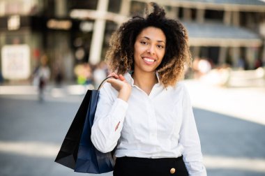 Confident young afro american female manager outdoor in a modern urban setting holding shopping bag