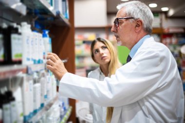 İki eczacı, kadın ve erkek, rafta bir ürün arıyorlar.