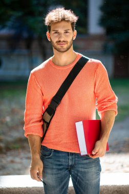 Üniversite bahçesinde gülümseyen bir öğrenci.