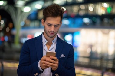 Geceleri şehirde yürürken cep telefonunu tutan bir adam.
