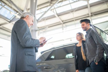 Satıcıyla konuşan ve yeni arabalarını galeride seçen mutlu bir aile.
