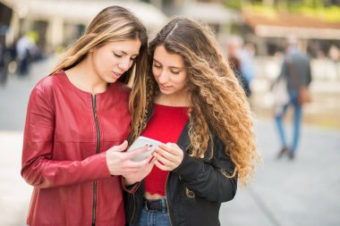 Şehirde cep telefonu kullanan gülümseyen kadınlar.