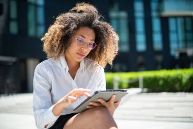 Afro-Amerikan iş kadını iş ortamında dijital tabletini açık havada kullanıyor.