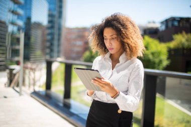 Afro-Amerikan iş kadını iş ortamında dijital tabletini açık havada kullanıyor.