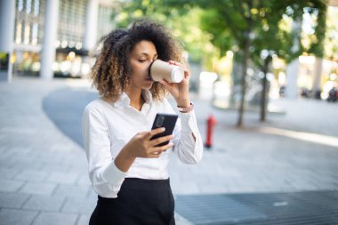 İş ortamında kahve içerken cep telefonunu kullanan Afrikalı Amerikalı iş kadınının portresi.