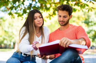 İki öğrenci açık hava bankında birlikte ders çalışıyor.