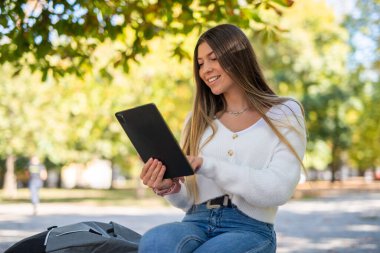 Parktaki bankta dijital tablet kullanan genç bir kadın.