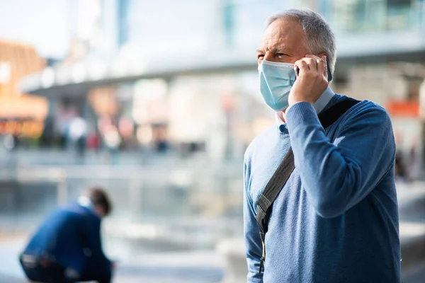 シニアマスクの男が街の広場で電話で話してる — ストック写真