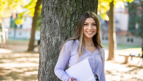 Студентка Колледжа Держит Свои Заметки Открытым Небом Возле Дерева — стоковое фото