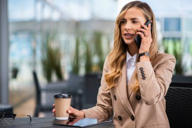 Genç sarışın iş kadını bir kafede telefonla konuşuyor.