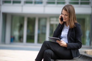 İş kadını tabletini kullanırken telefonda konuşuyor.