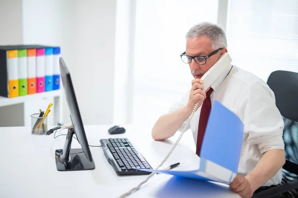 デスクトップコンピュータを使用している間に電話で話しているビジネスマン — ストック写真
