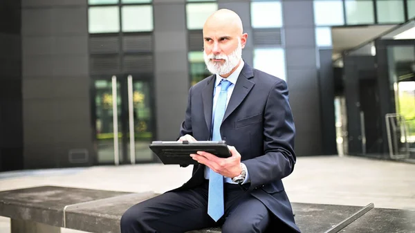 現代都市のベンチの屋外に座っている彼のタブレットを使用してスタイリッシュなマネージャー — ストック写真