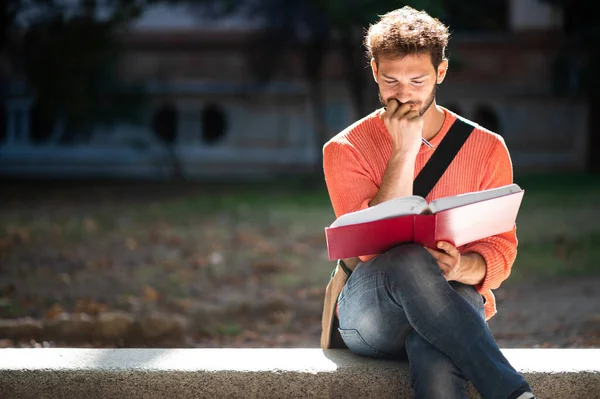 公園のベンチで本を読んでハンサムな若い男 — ストック写真