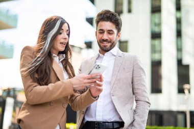 Genç iş kadını bir meslektaşına akıllı telefonunu gösteriyor.