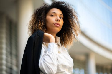 Kendine güvenen genç Afro-Amerikan bayan yönetici dışarıda modern şehir ortamında ceketini tutuyor.