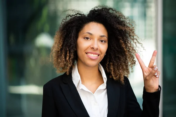 自信を持って若いですアフロアメリカの女性マネージャー屋外笑顔と彼女の指で勝利のサインを行います — ストック写真