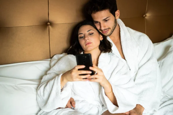 stock image Young couple in bed sharing a smartphone