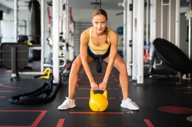 Spor salonunda kettlebell topu kullanan bir kadın.
