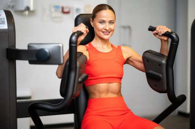 Spor salonunda göğüs pres makinesi kullanan bir kadın.