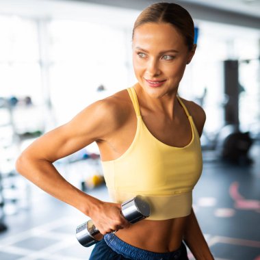 Beautiful young woman lifting dumbbells in a gym