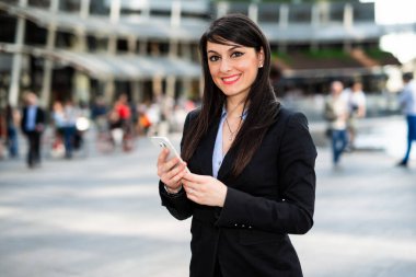 Güzel genç bayan yönetici dışarıda akıllı telefonunu kullanıyor.