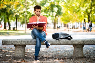 Yakışıklı genç adam parkta bankta kitap okuma