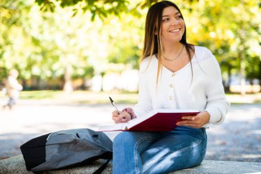 Güzel bir üniversite öğrencisi parkta bir bankta kitap okuyor.