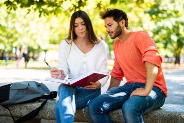 İki öğrenci açık hava bankında birlikte ders çalışıyor.