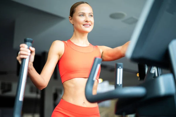 stock image Woman exercising in a gym with an elliptical cross trainer