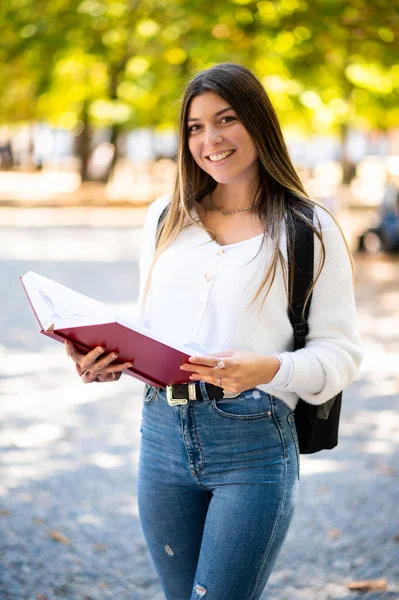 Parkta bir kitap tutan ve gülümseyen kız öğrenci